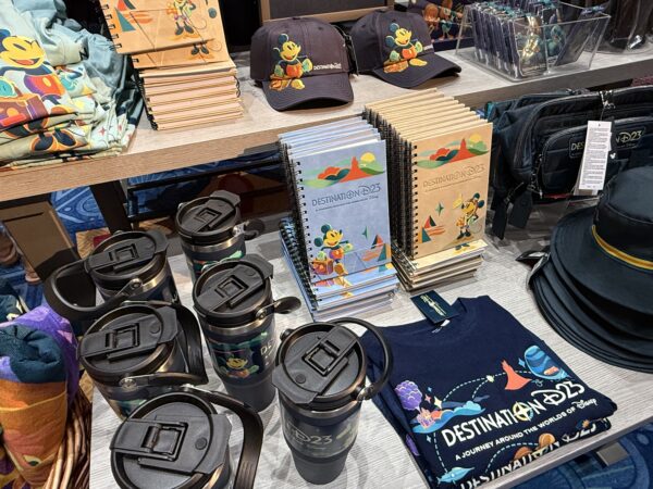 Colorful D23 merchandise include cups, t-shirts, notepads, and hats.